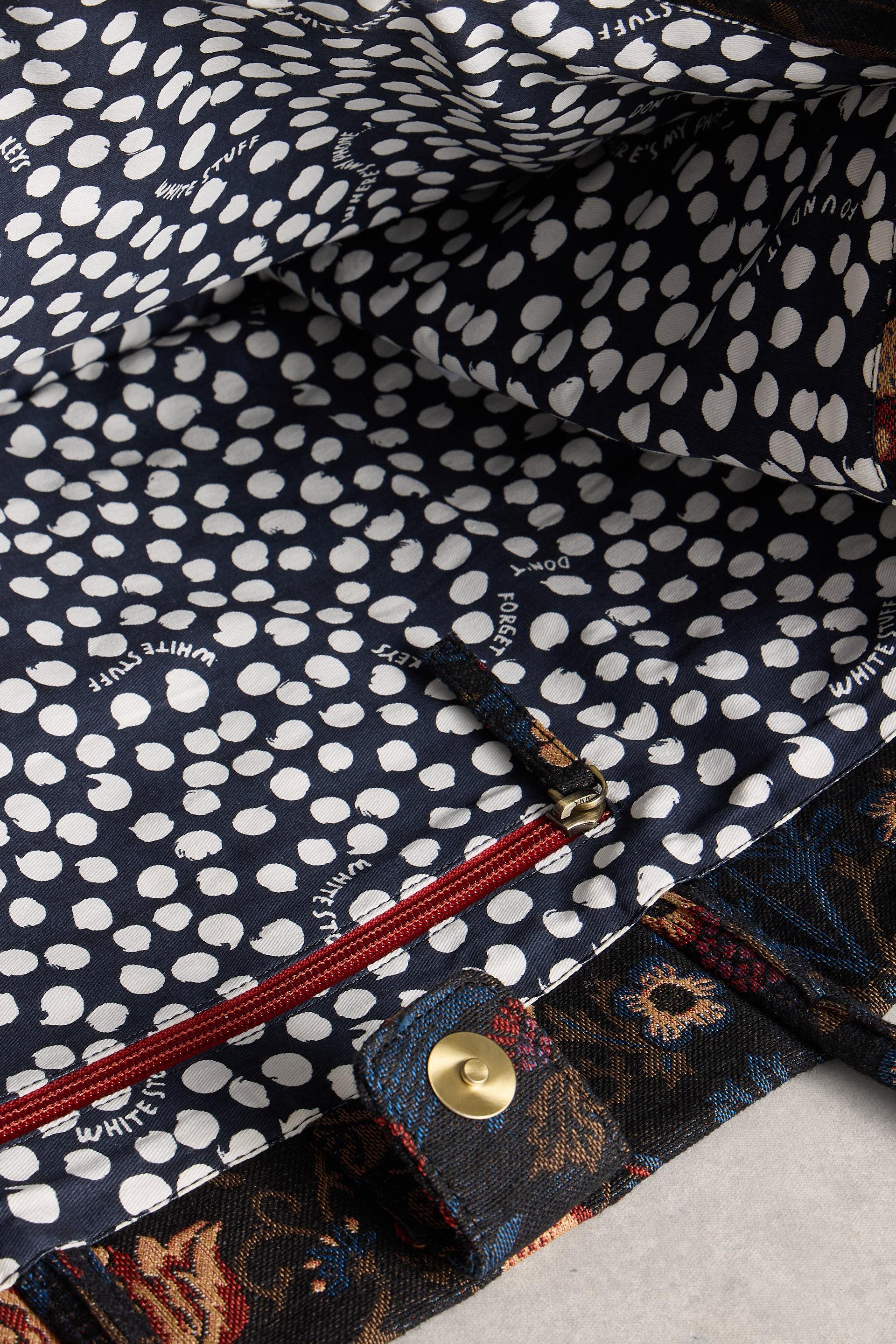 Close-up of a navy blue fabric with white polka dots and a floral pattern on a red zipper.