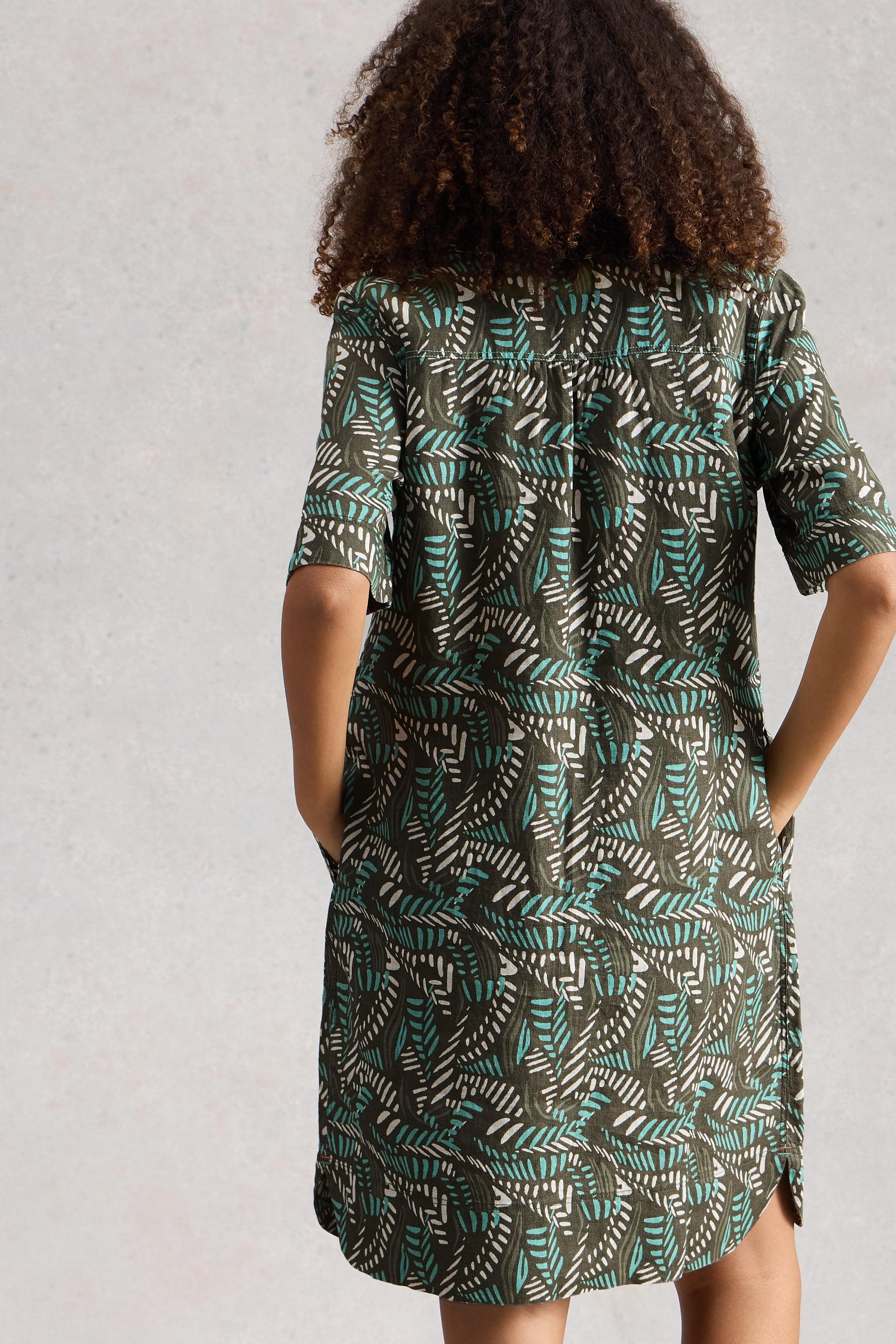 Model wearing a patterned linen dress with their back to the camera on a plain background