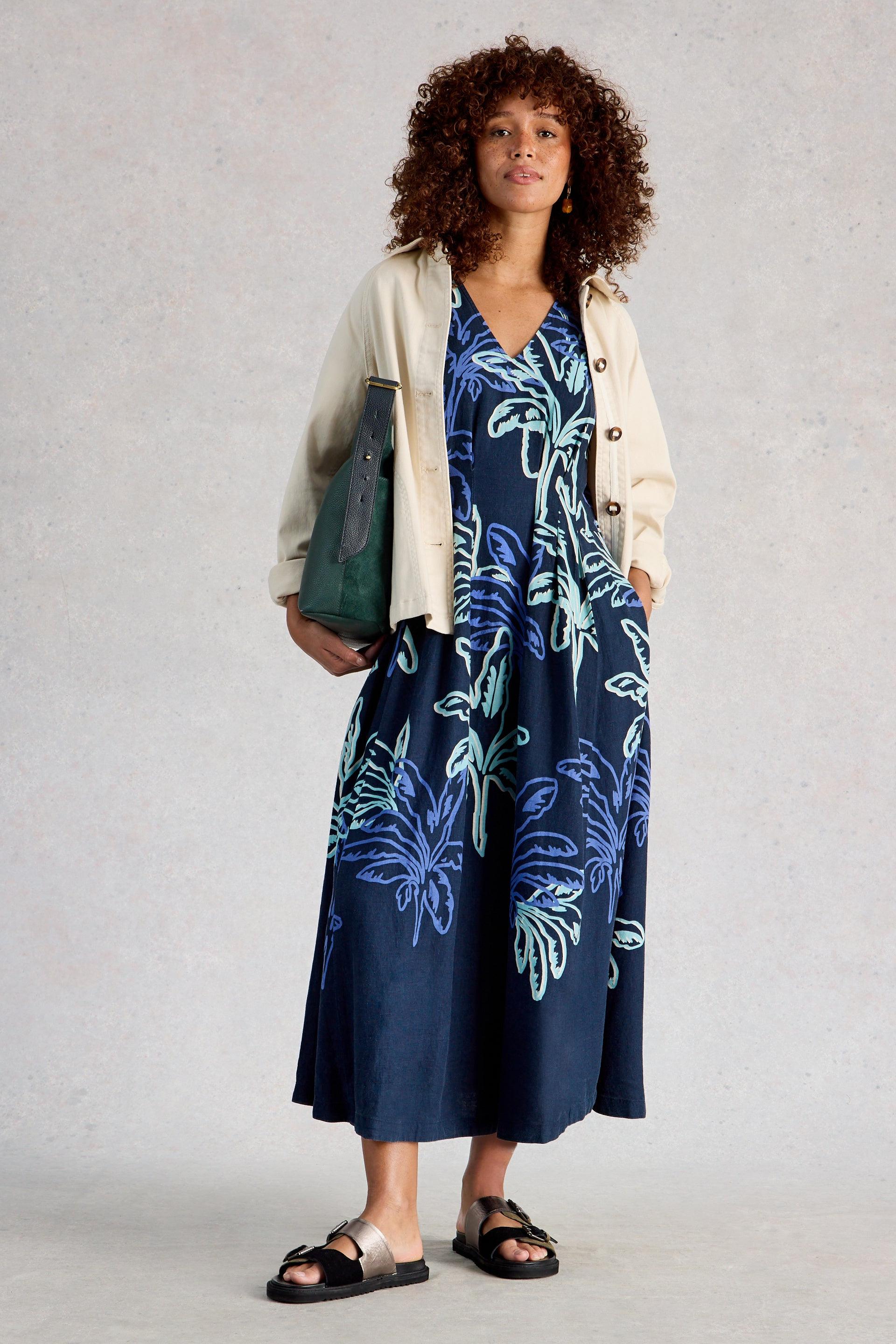 Woman wearing a navy floral linen dress with a beige cardigan against a plain background
