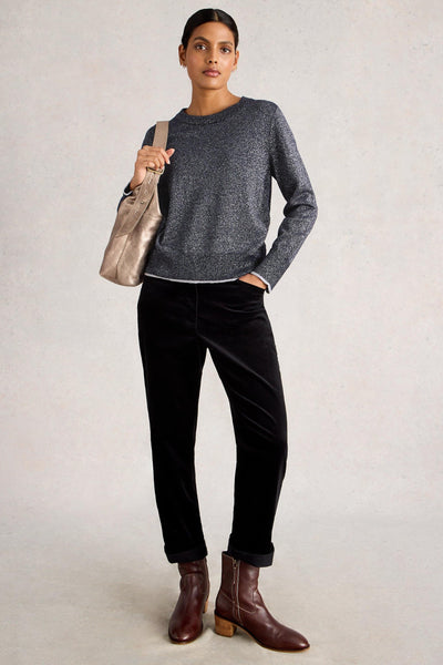 Woman wearing a gray wool sweater, black pants, and brown boots, holding a beige bag on a light background