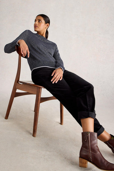 Woman sitting on a wooden chair wearing a gray organic cotton sweater, black pants, and brown boots.