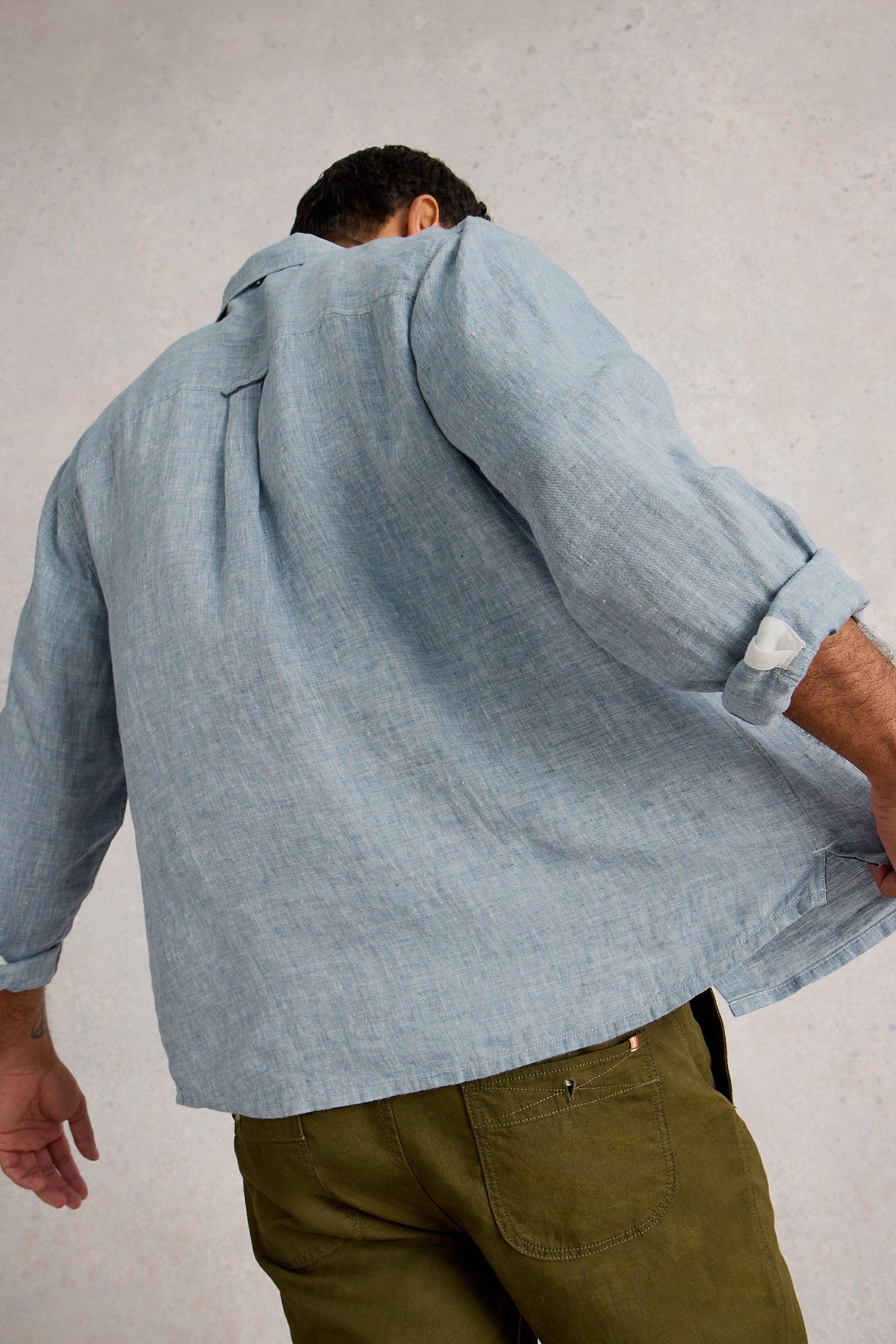 Person wearing a light blue linen shirt and green pants on a plain background