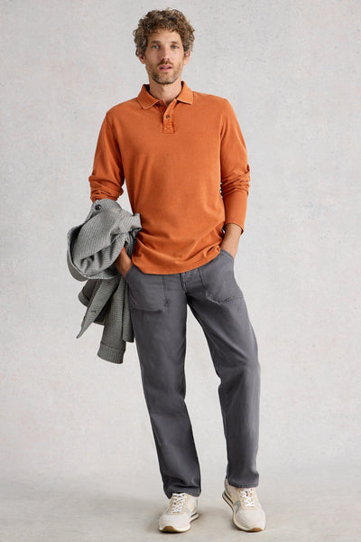 Man standing wearing fairtrade cotton long sleeve orange polo styled with grey chino trousers and white sneakers