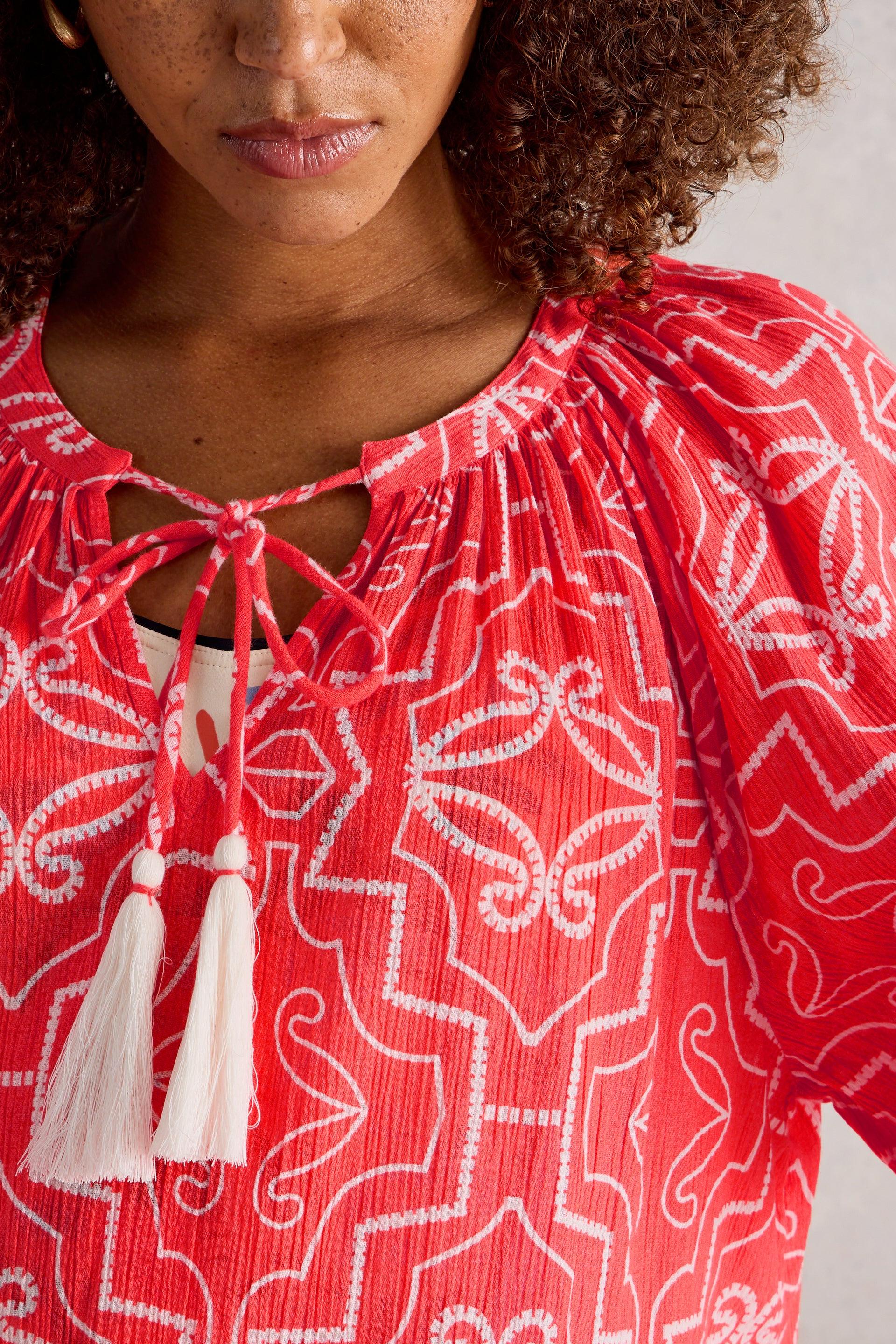 Red patterned cover up with white tassels worn by a model