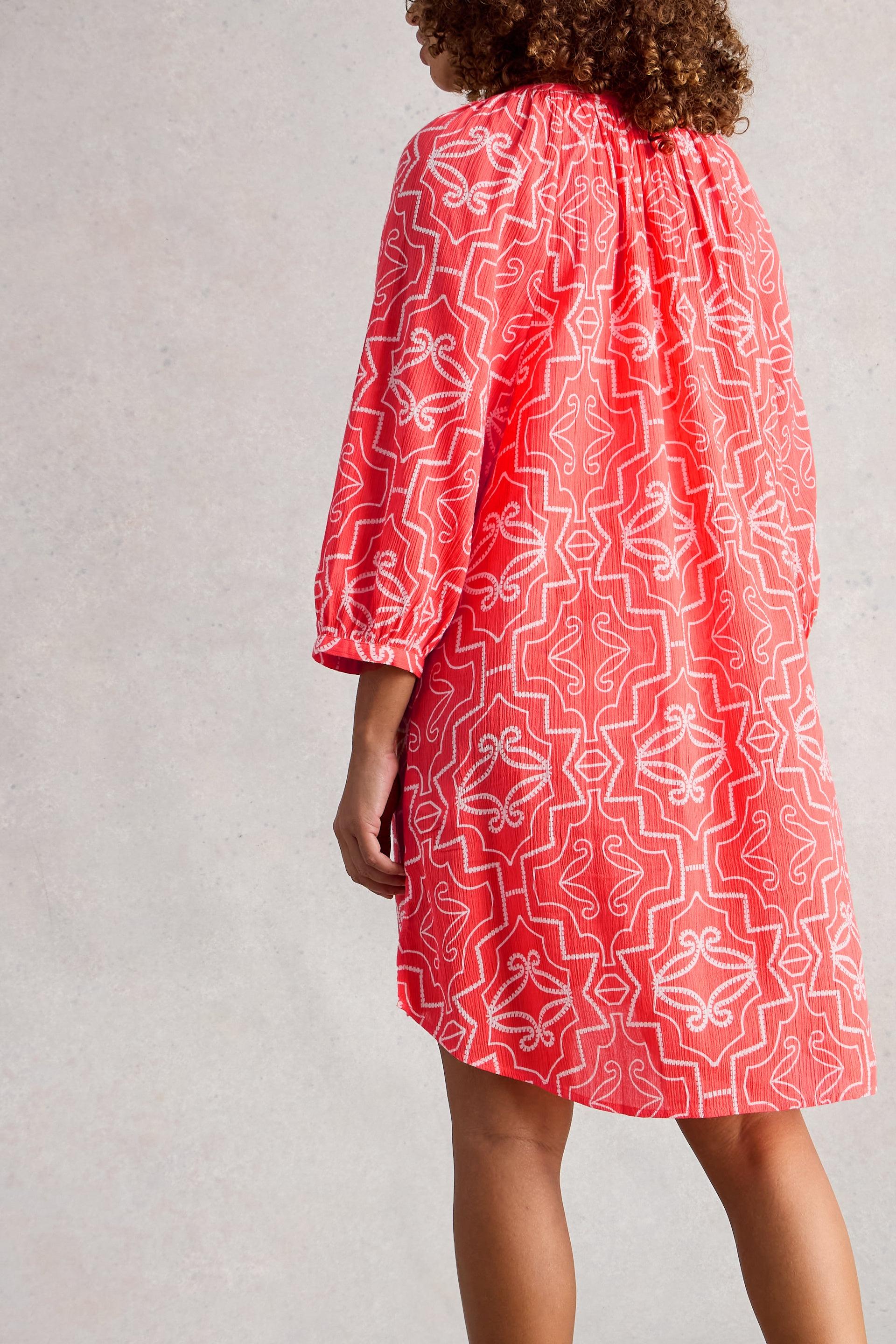 Red coverup with white patterns worn by a model on a plain background