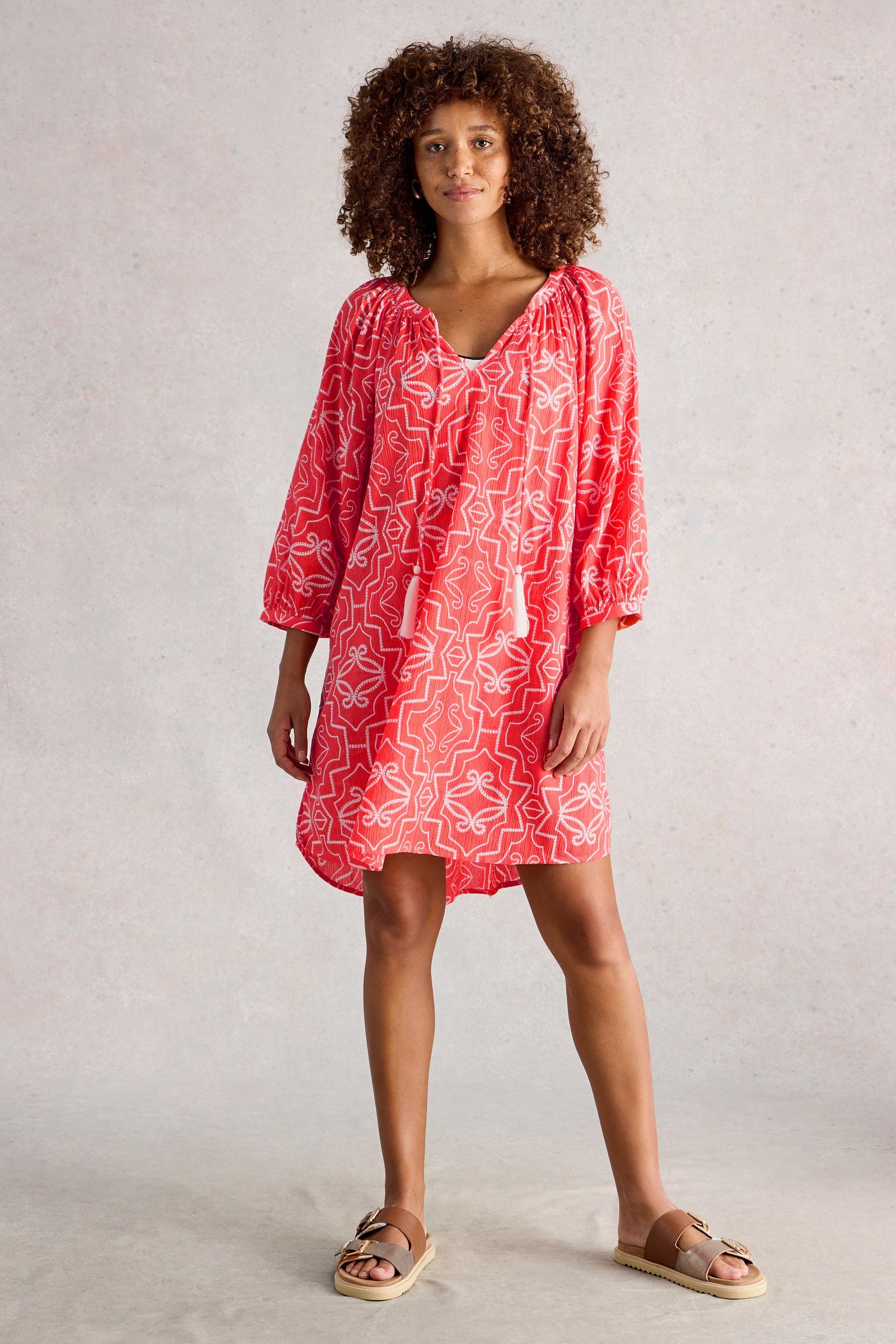 Woman wearing a red patterned dress against a plain background