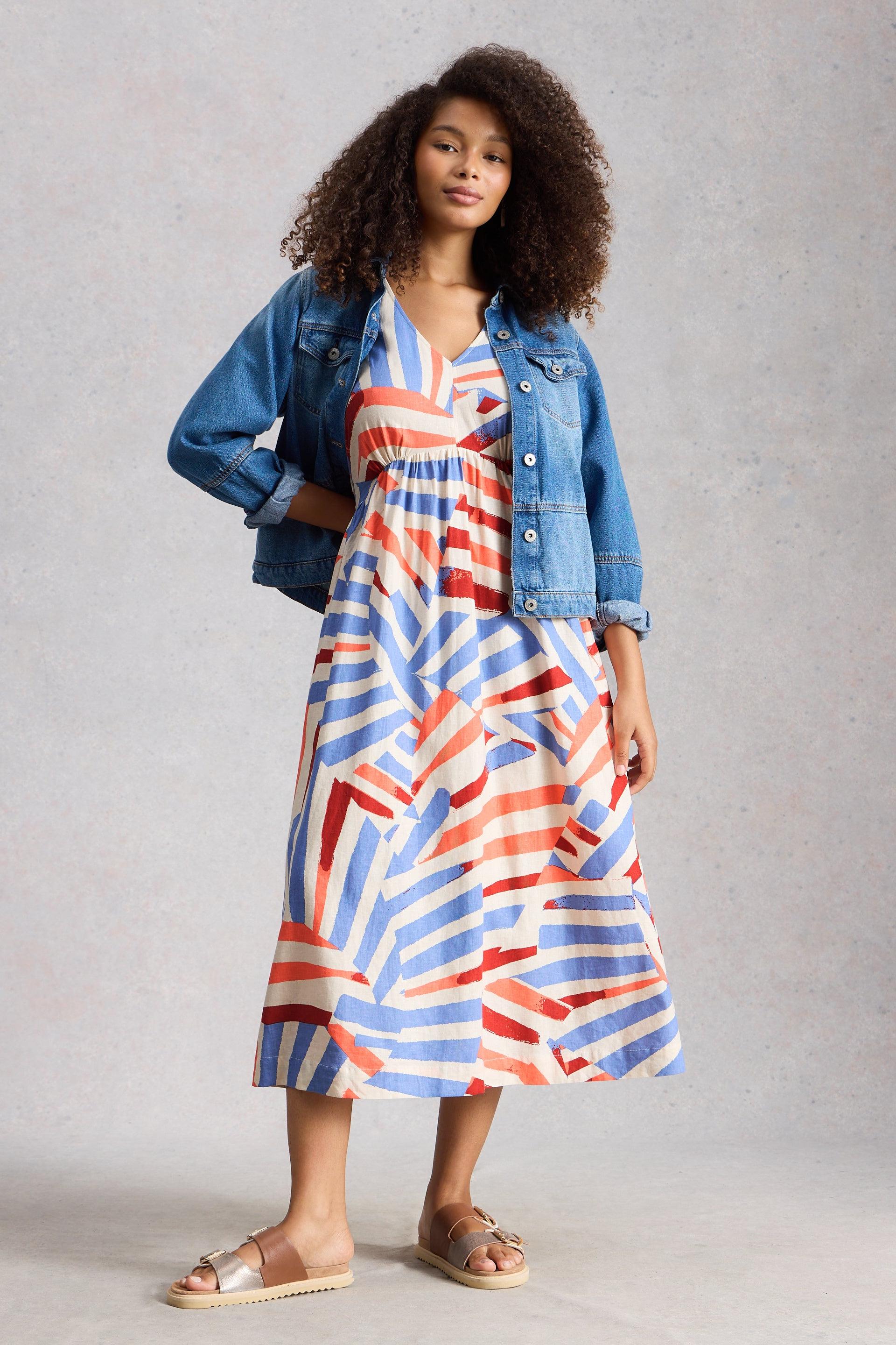 Woman wearing a colorful linen dress with a denim jacket on a plain background
