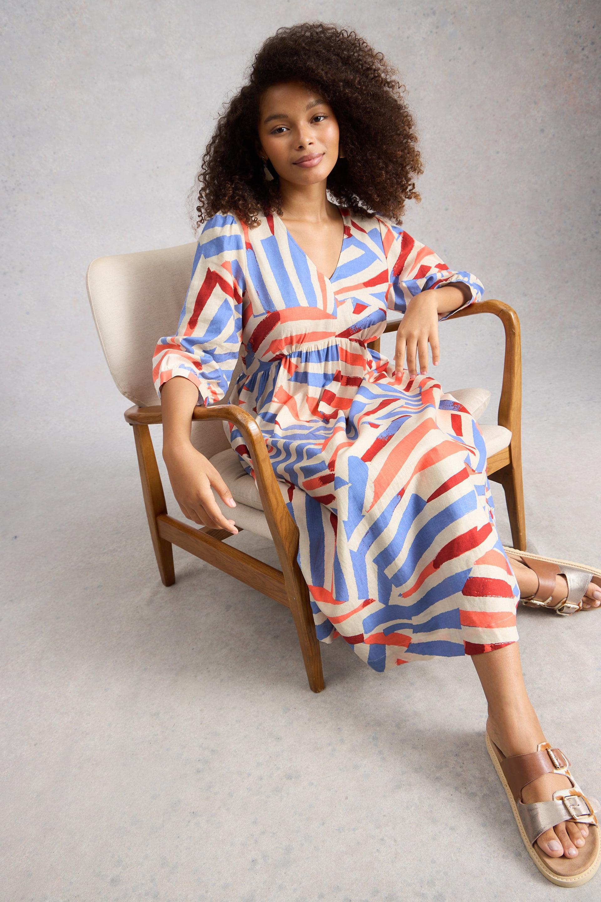 Woman in a colorful linen midi dress sitting on a chair against a gray background