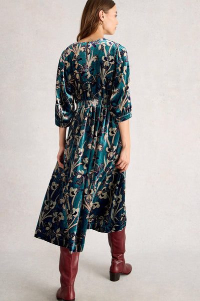Woman wearing a floral dress with long sleeves and maroon boots on a plain background