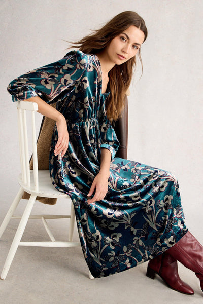 Woman sitting on a chair wearing a floral velvet dress and red boots.