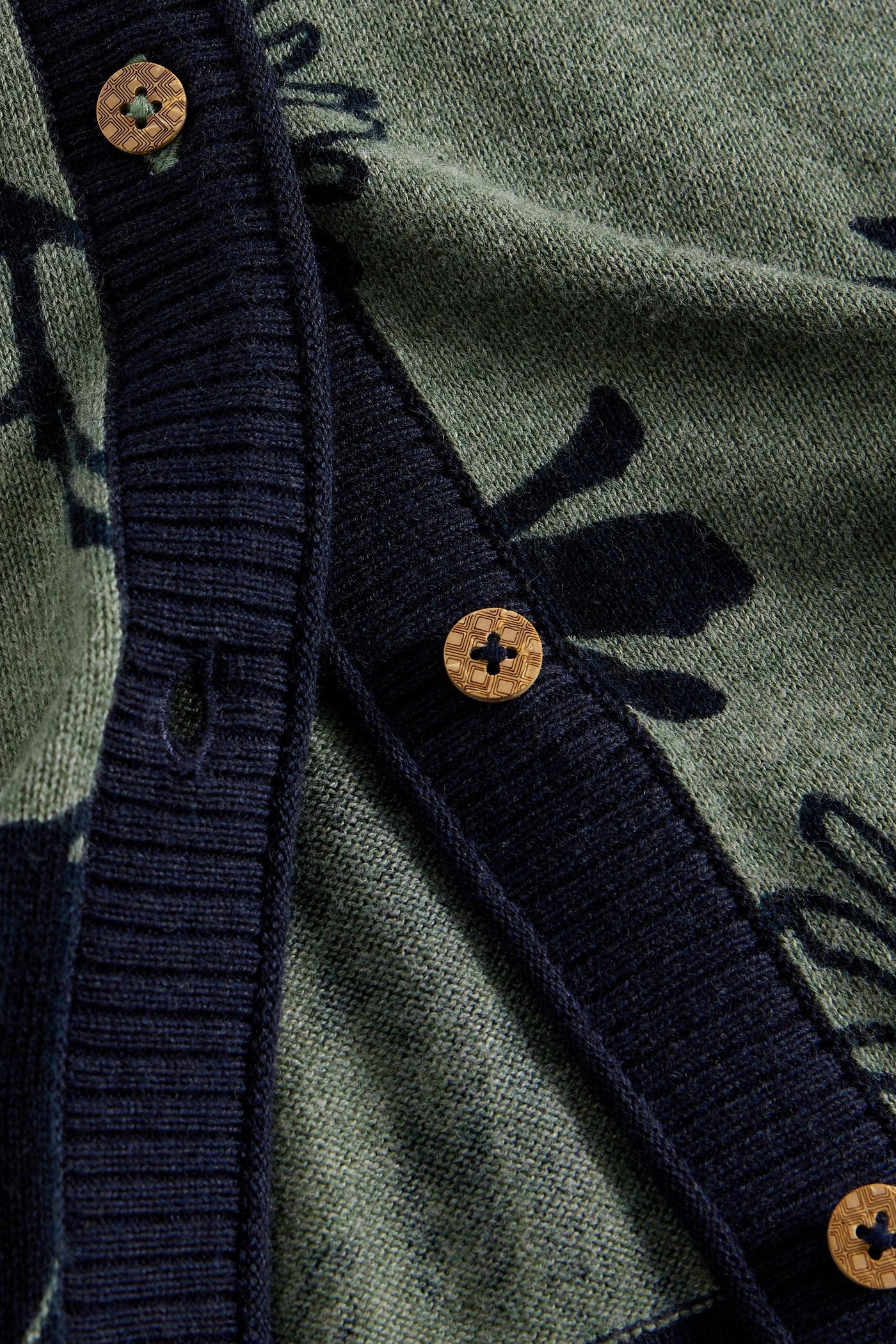 Close-up of the front of a green and navy floral cardigan showing wooden buttons and navy ribbed trim