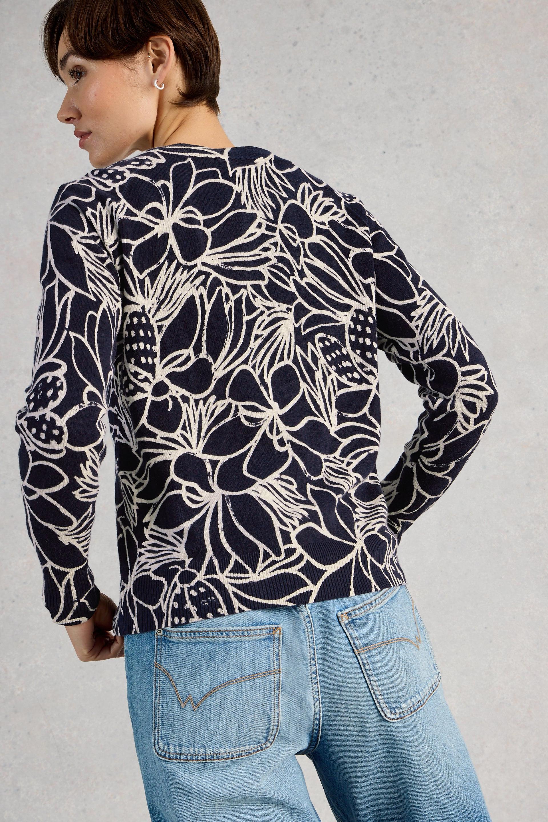 Person wearing a navy floral patterned cardigan and light blue jeans against a gray background