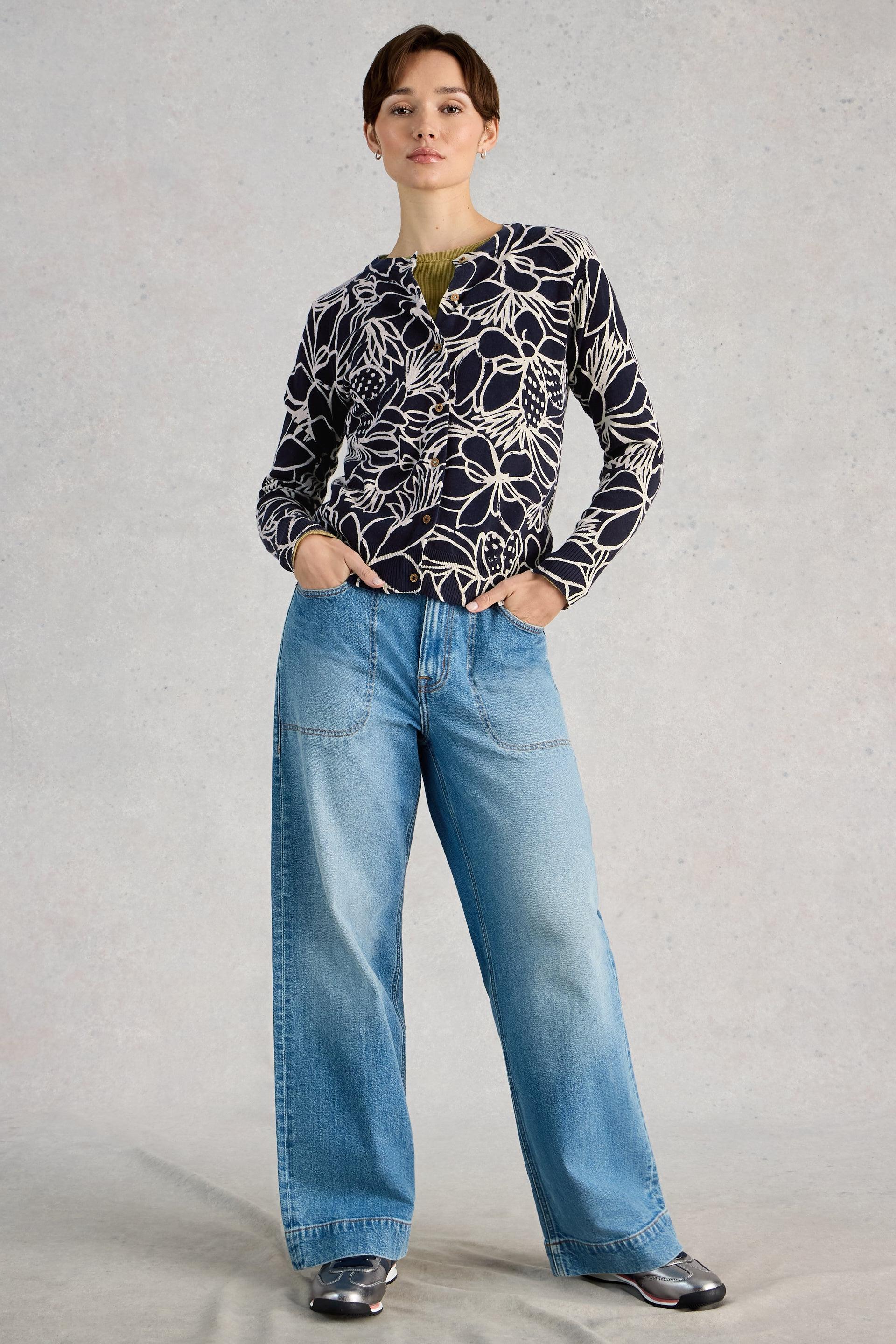 Person wearing a patterned organic cotton cardigan and blue jeans on a plain background