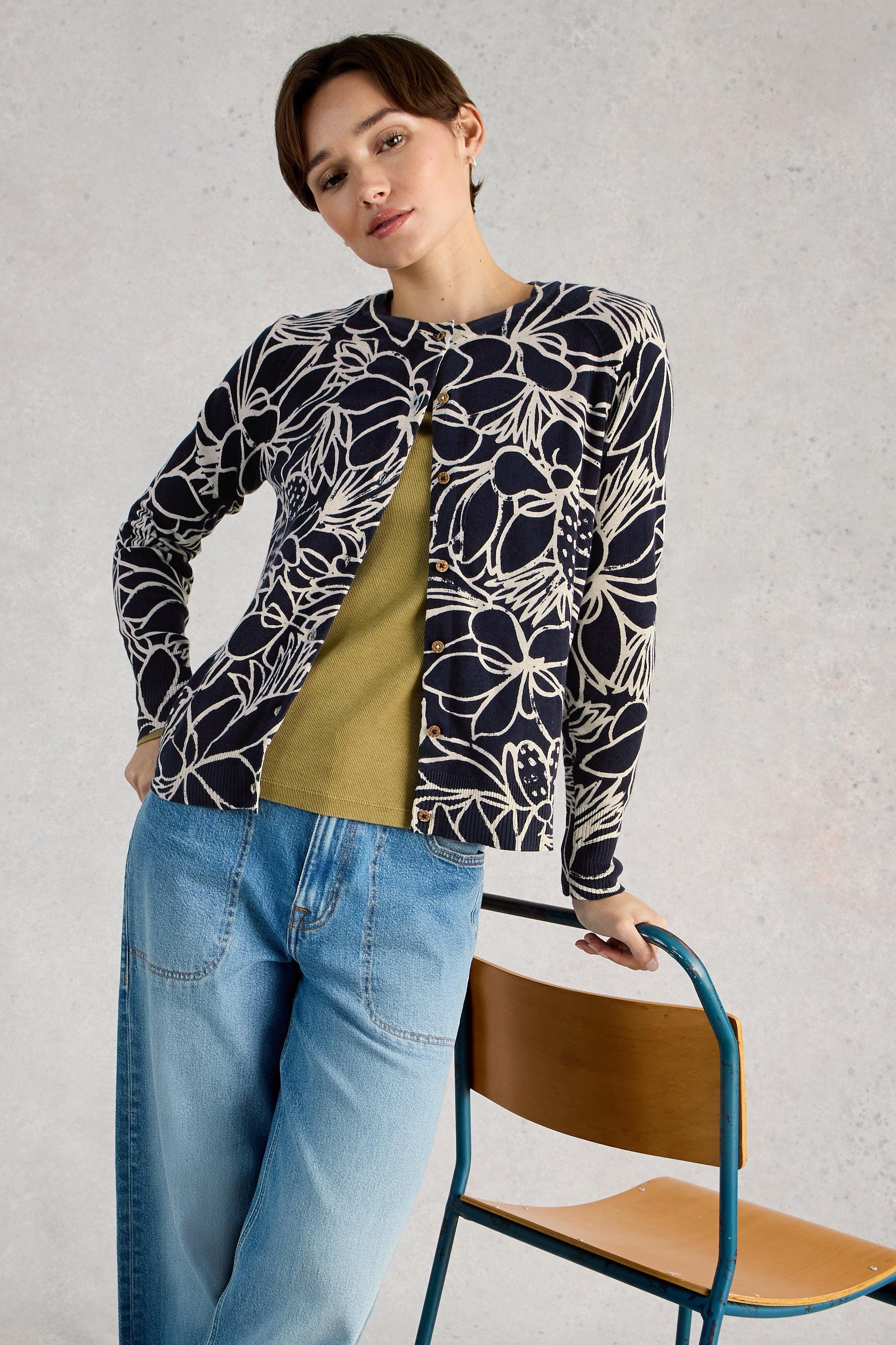 Woman wearing a patterned organic cotton cardigan over a green shirt with blue jeans, standing against a plain background.
