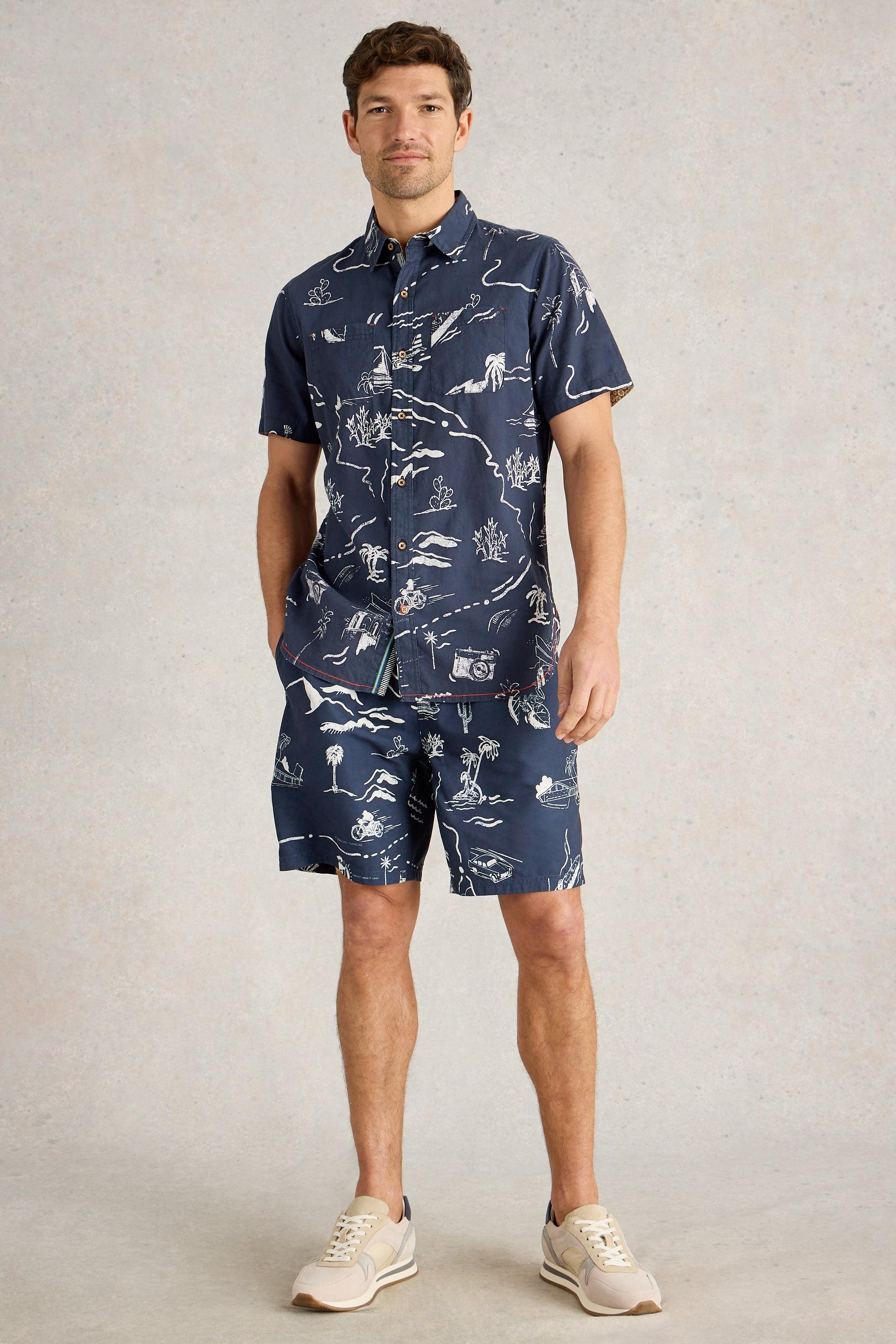 Model wearing navy beach shorts paired with matching shirt and white trainers.