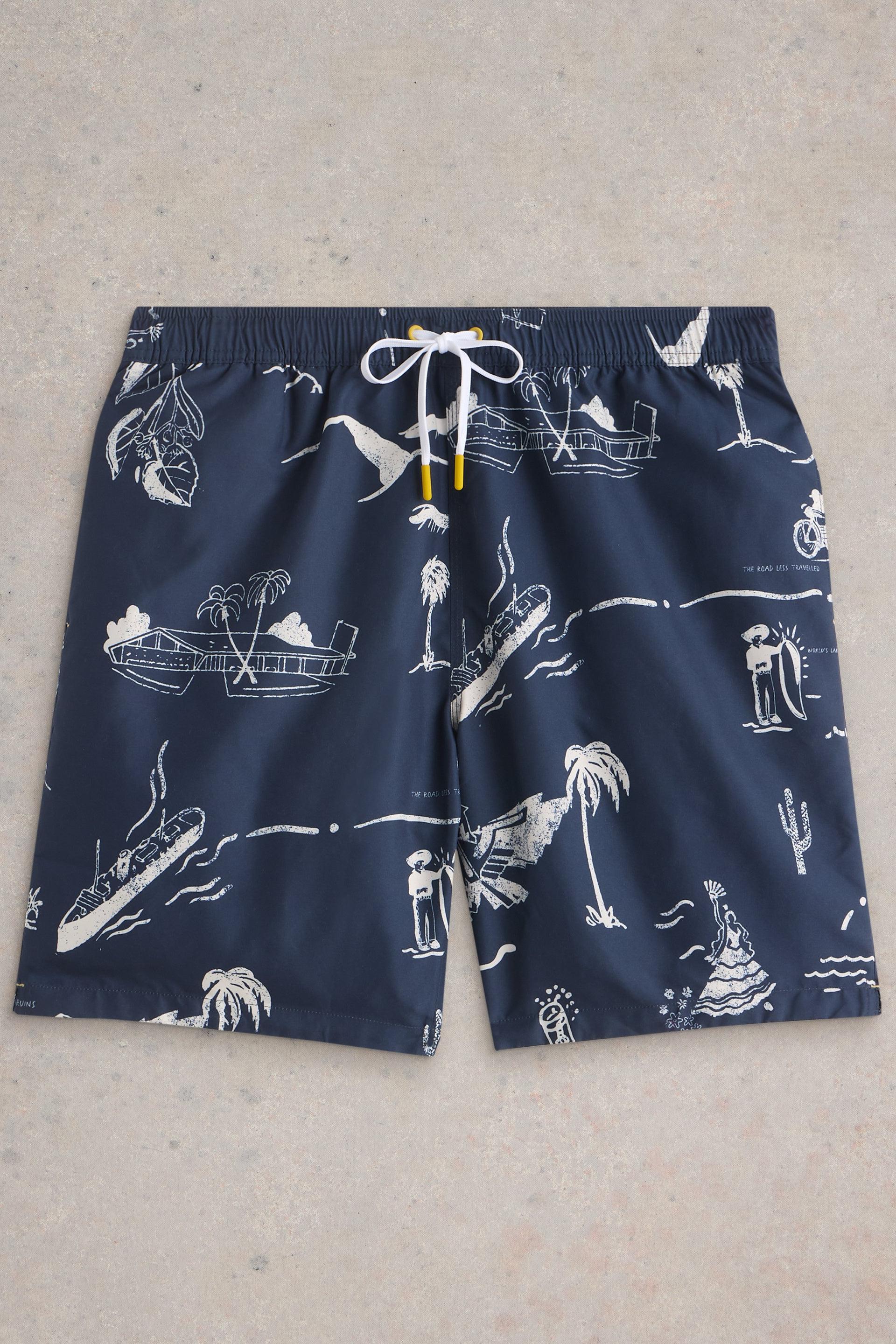 Navy beach shorts with a tropical map print laid flat on neutral background.