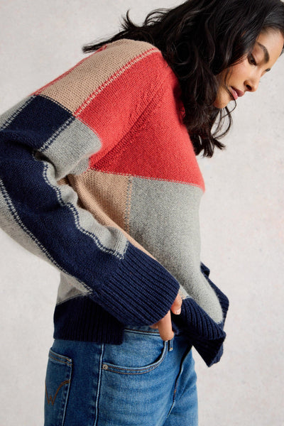 Person wearing a colourful patchwork wool sweater with a neutral background