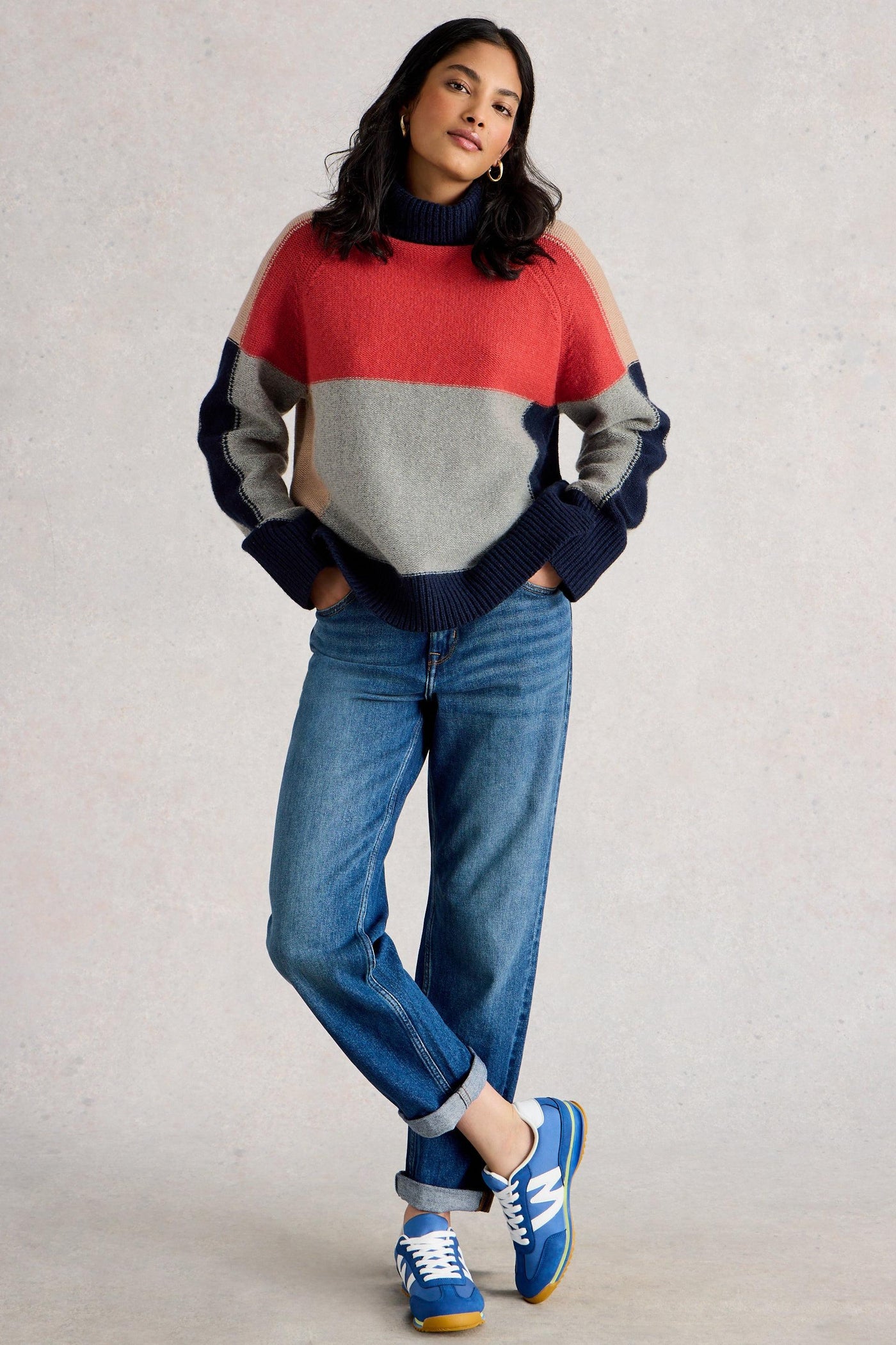 Woman wearing a colorful organic cotton sweater and blue jeans against a plain background
