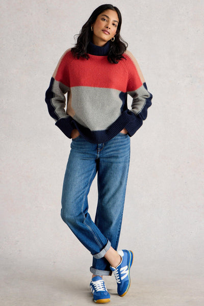 Woman wearing a colorful organic cotton sweater and blue jeans against a plain background