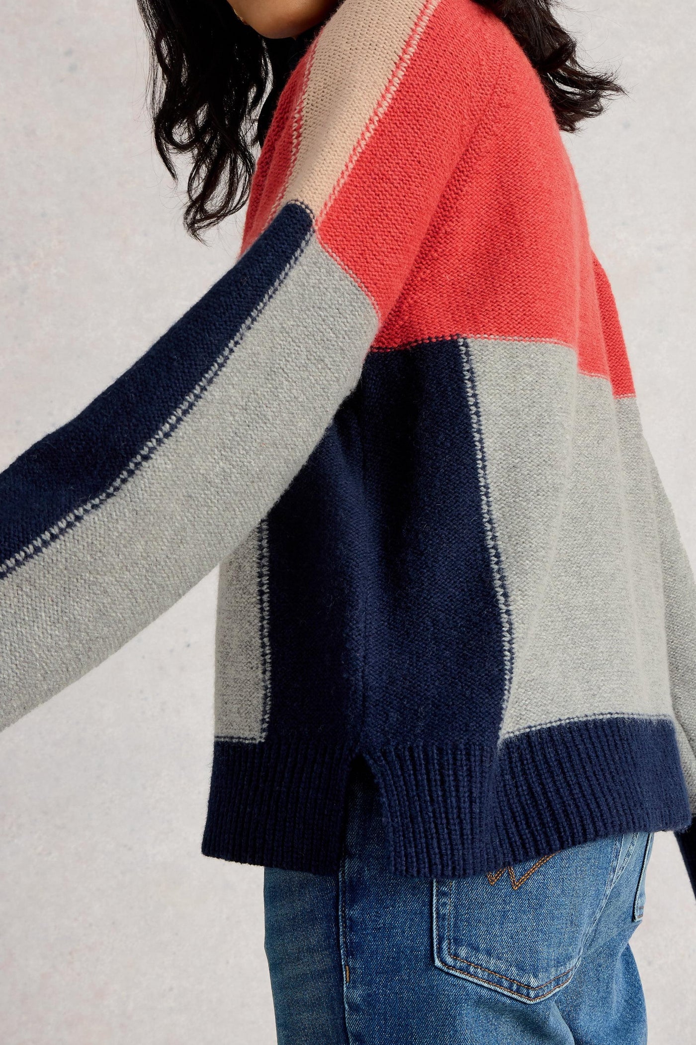 Colour-blocked wool sweater with red, blue, and gray sections worn by a person on a light background