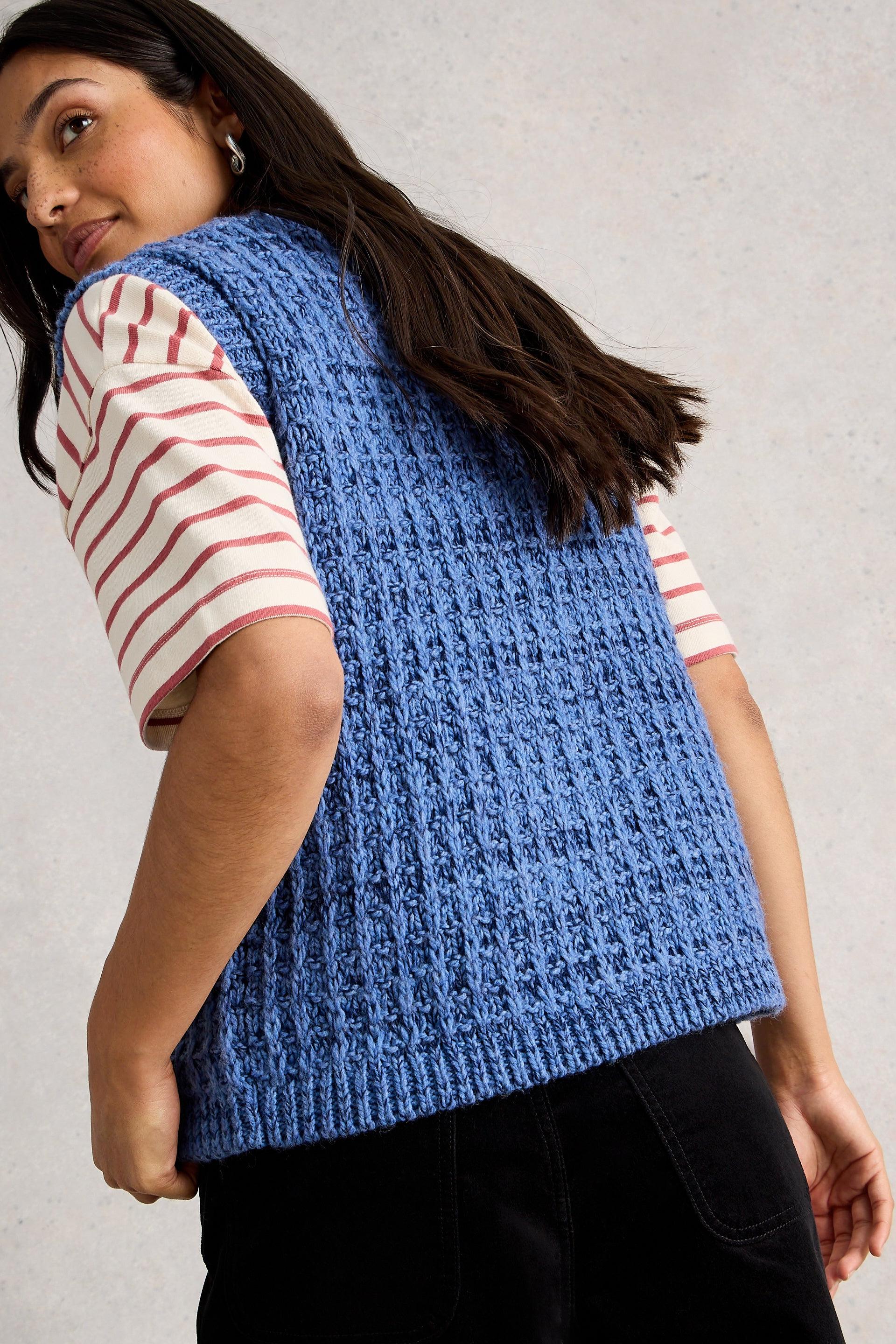 Woman wearing a blue knitted vest over a striped shirt against a plain background