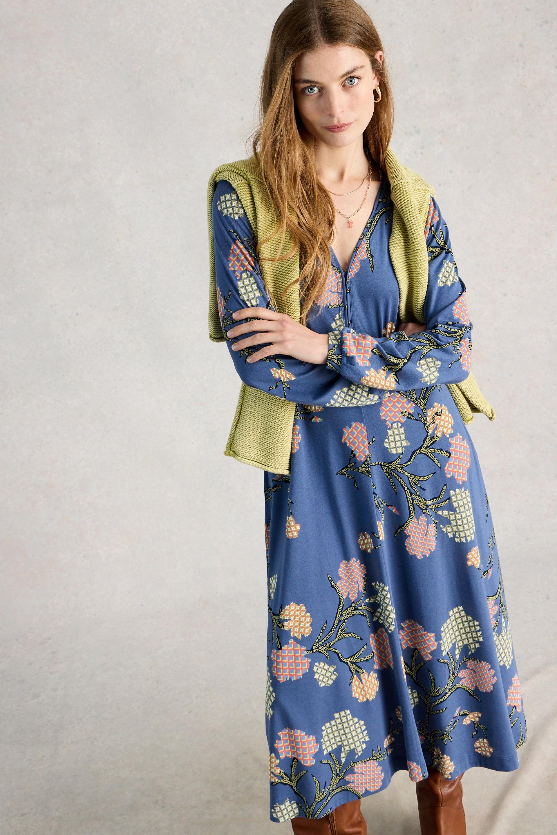 Woman wearing a blue organic cotton dress with a green jacket against a plain background