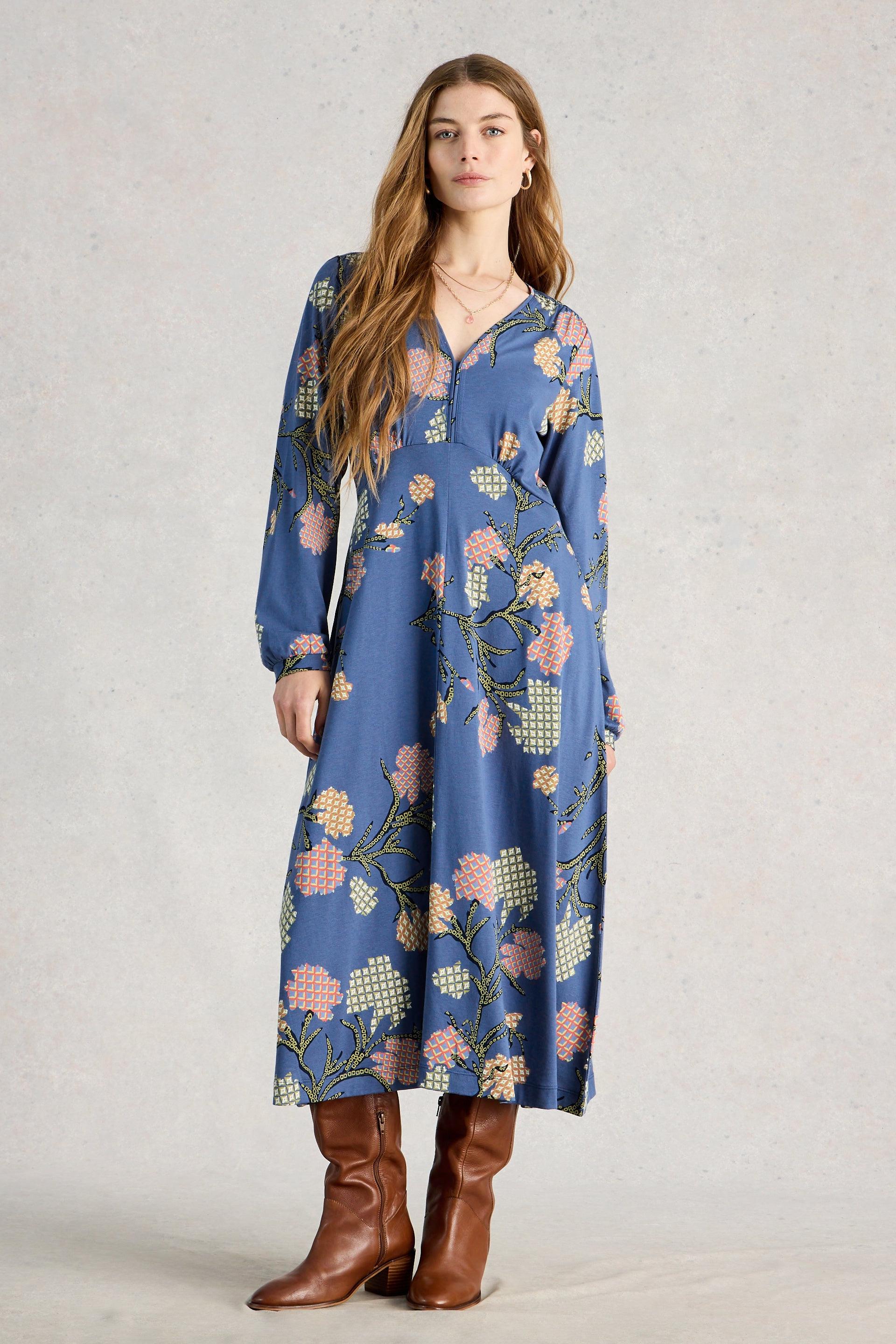 Woman wearing a blue floral dress with brown boots on a plain background