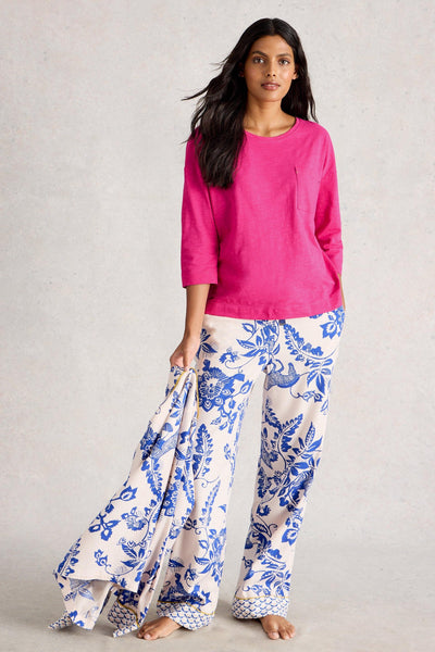 Woman wearing a pink top and blue floral pants on a neutral background