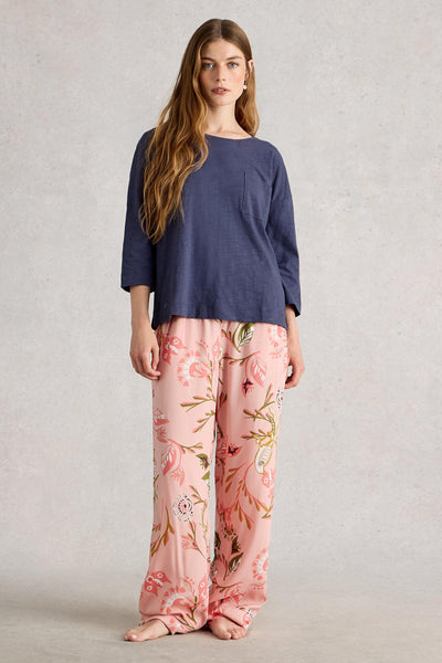 Woman wearing a navy pyjama top and pink floral pj bottoms on a plain background