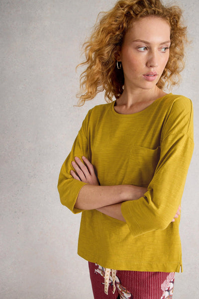 Woman wearing a mustard yellow organic cotton top with a plain background