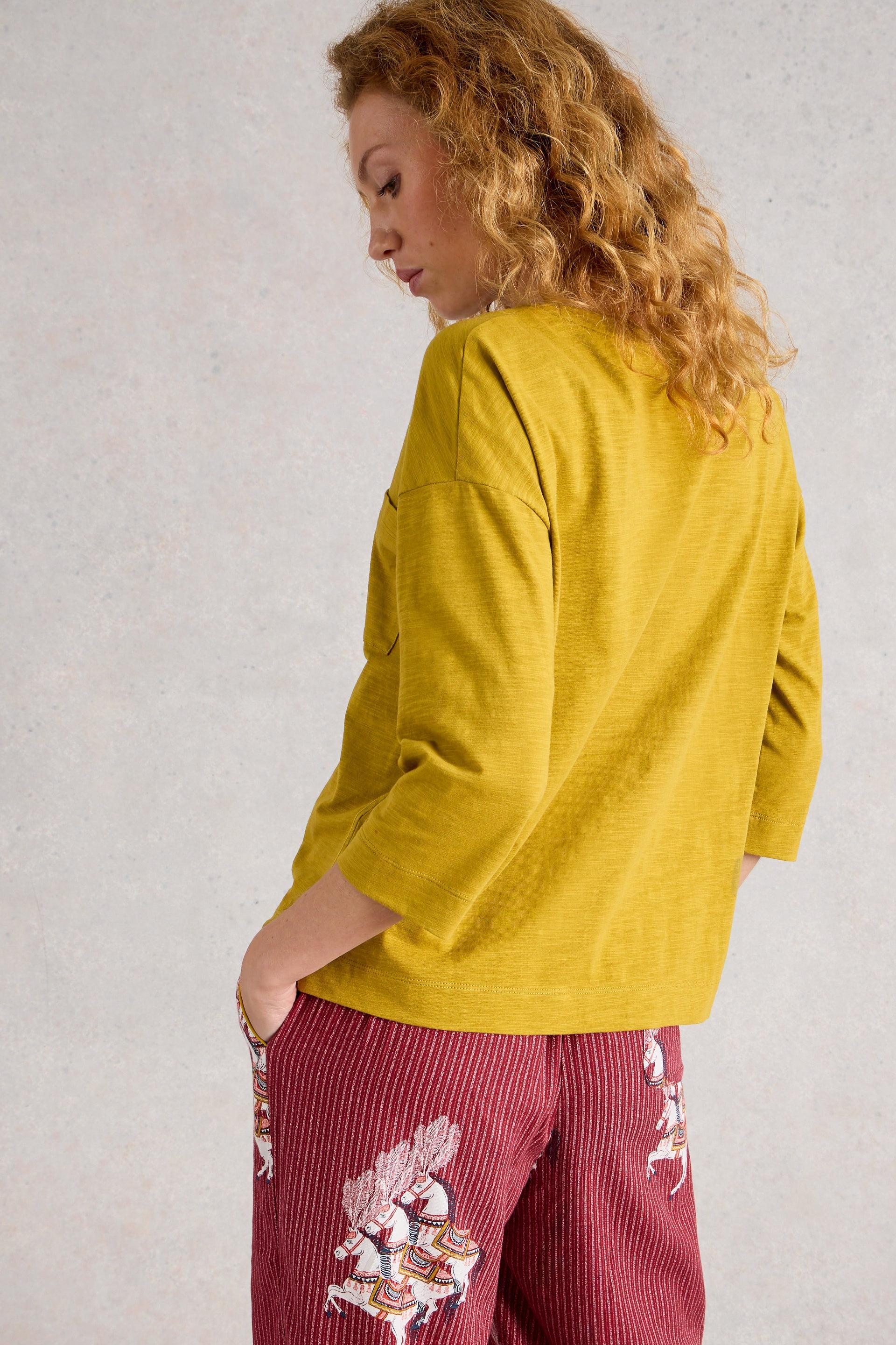 Woman wearing a mustard yellow top and red pants with floral patterns against a light gray background