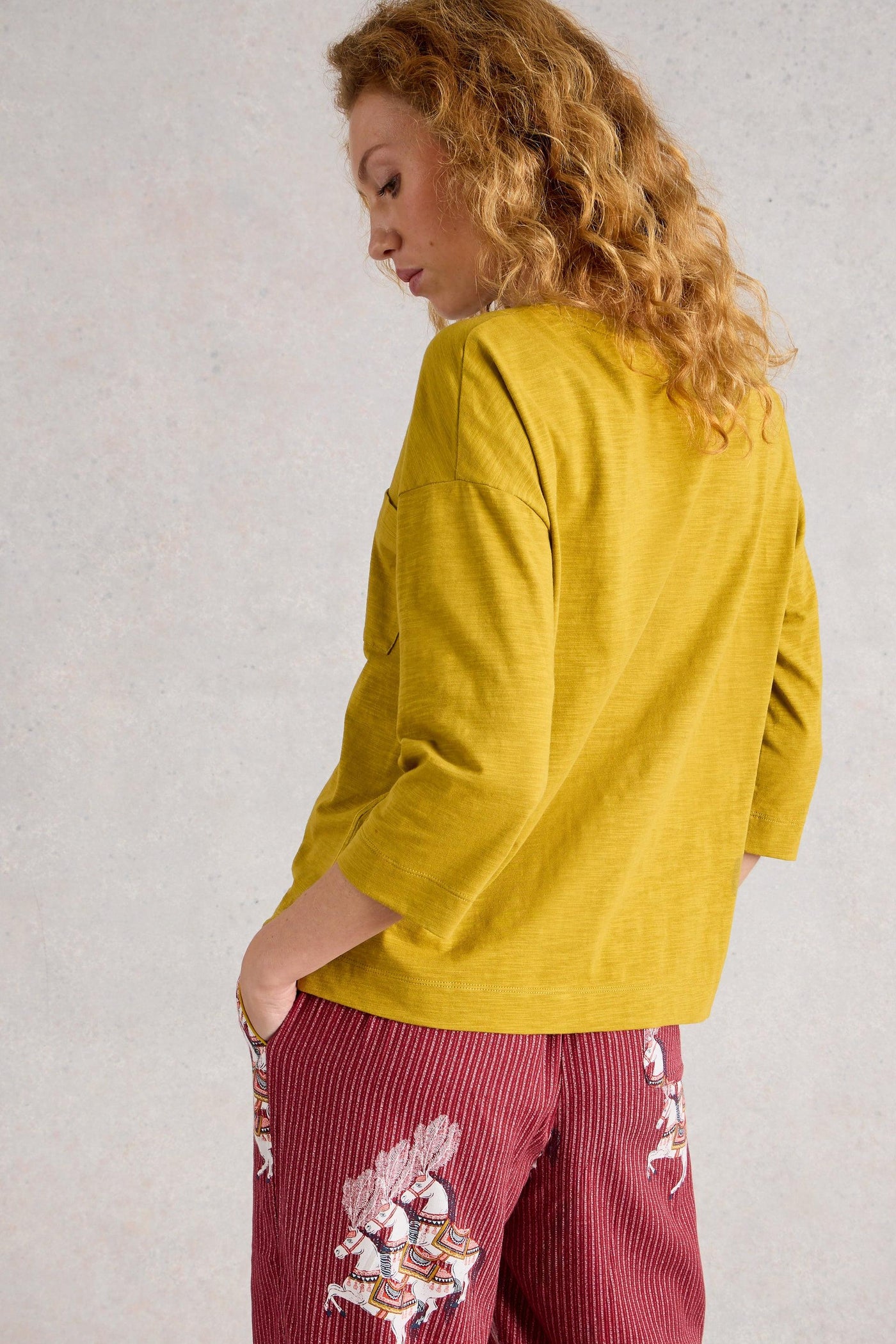 Woman wearing a mustard yellow top and red pants with floral patterns against a light gray background