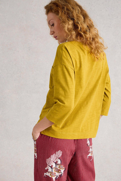 Woman wearing a mustard yellow top and red pants with floral patterns against a light gray background