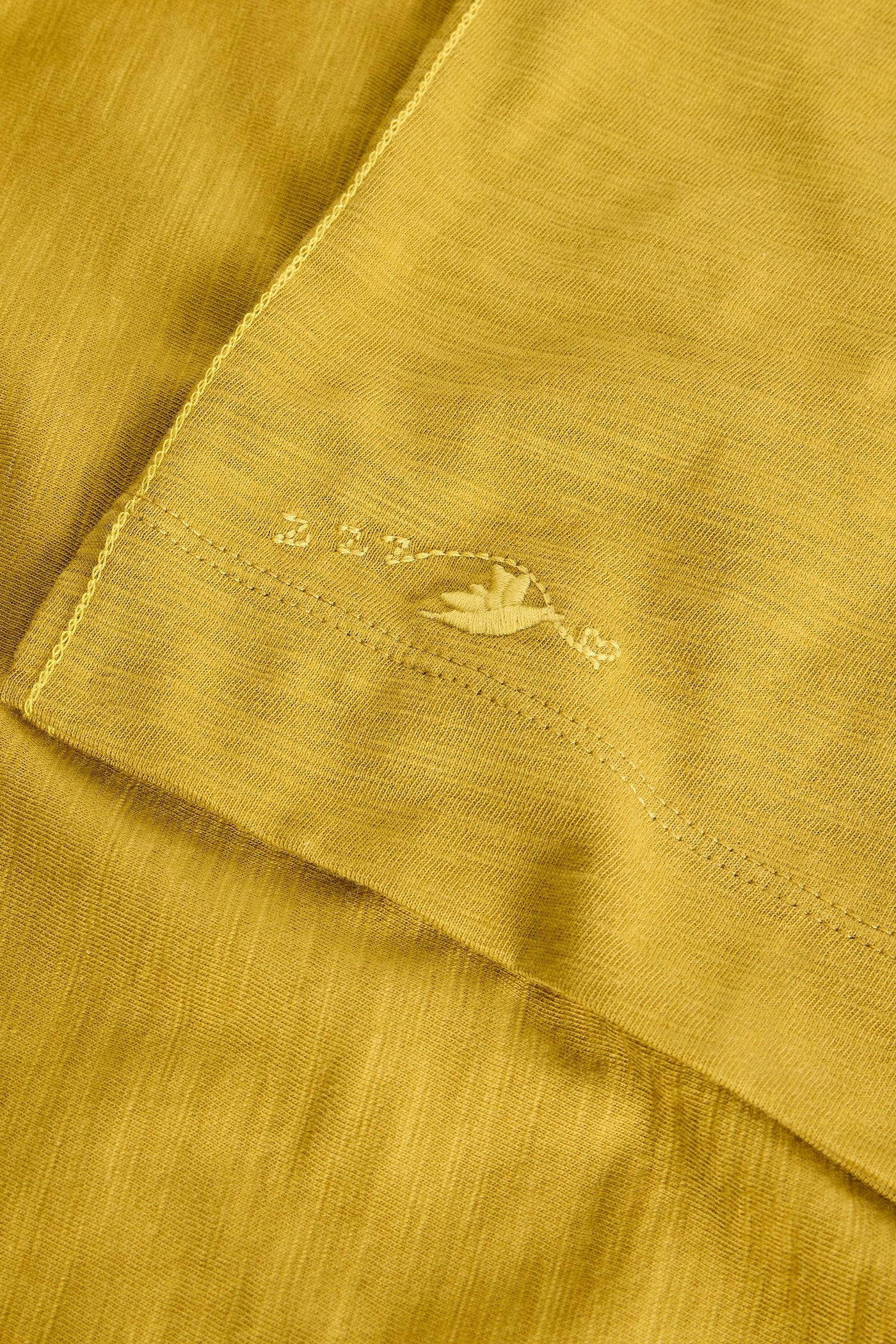 Close-up of a mustard yellow fabric with a small embroidered design.