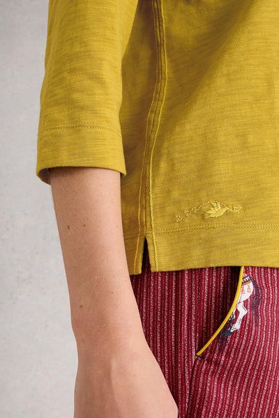 Yellow organic cotton shirt with a brand logo on a plain background
