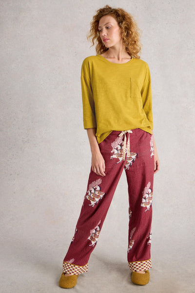 Woman wearing a mustard yellow top and red patterned pants on a plain background
