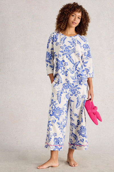 Woman wearing a blue floral organic cotton pajama set holding pink slippers against a neutral background