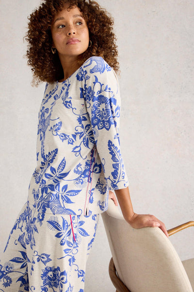 Woman wearing organic cotton pyjamas with a blue floral pattern sitting on a chair.