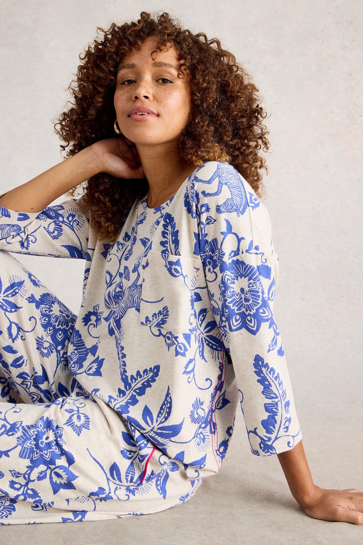 Woman wearing blue and white floral pyjamas sitting on a light gray background