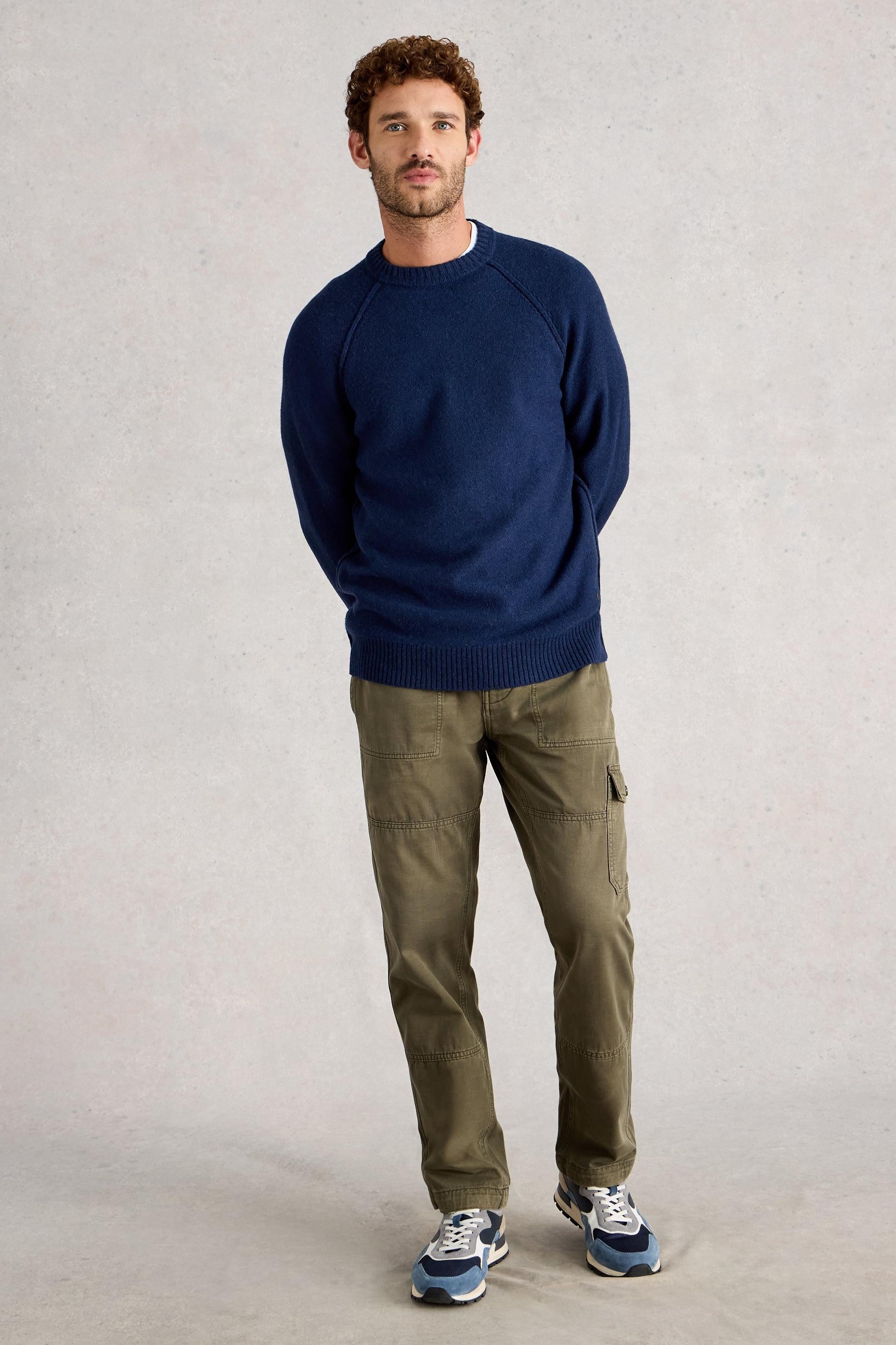 Man wearing a navy lambswool sweater and olive pants against a plain background