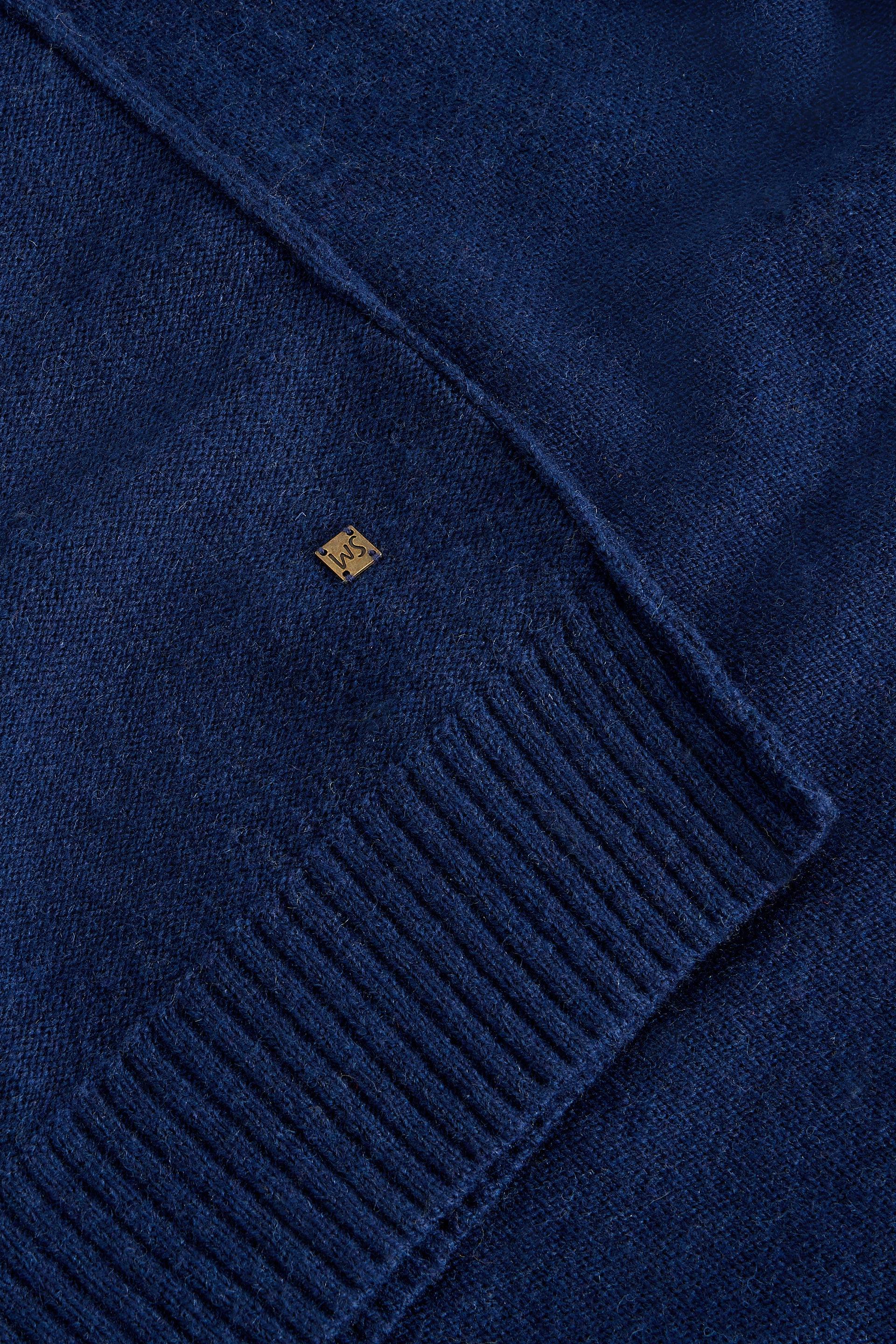 Close-up of a blue wool jumper with a brand logo on a matching blue background