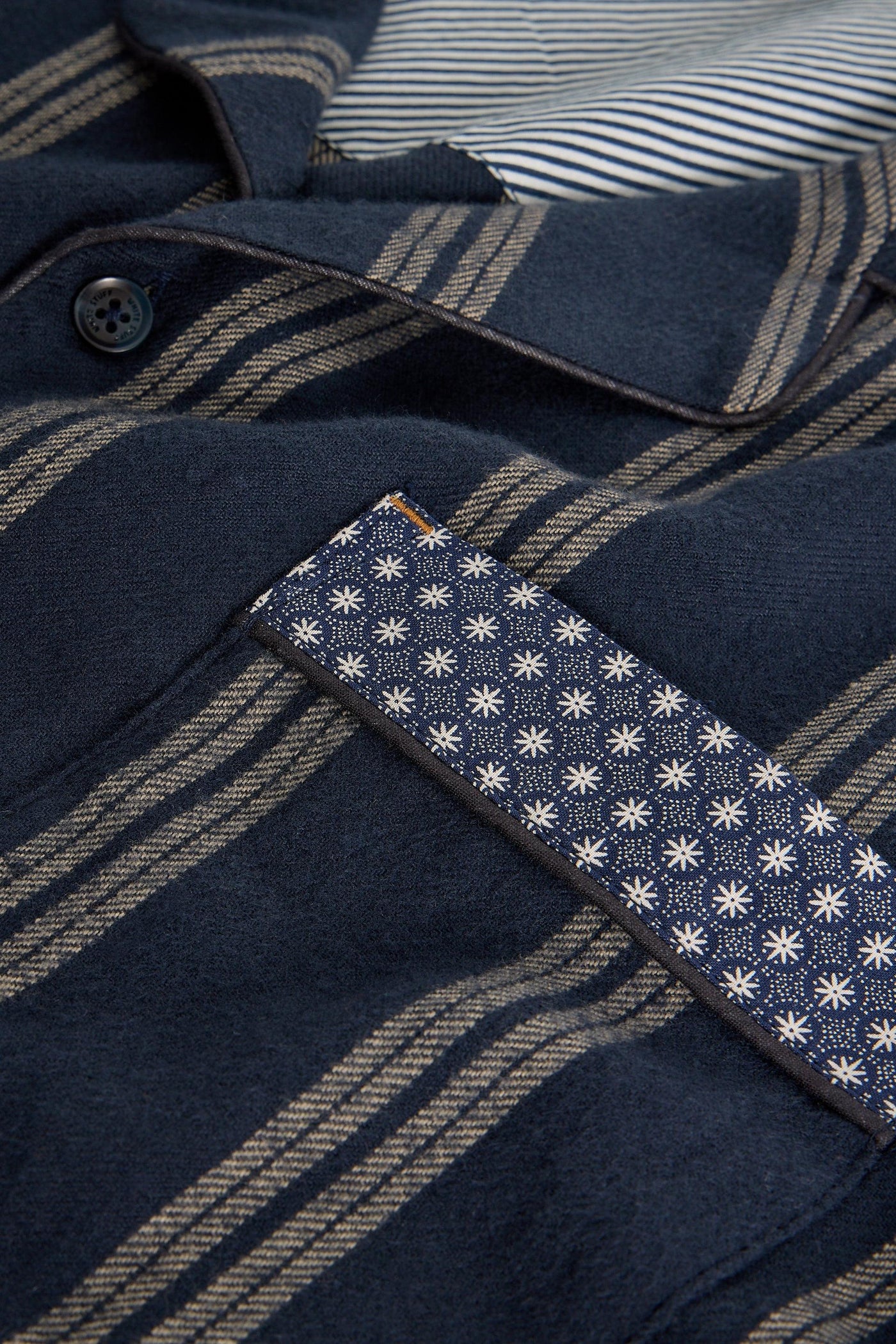 Close-up of a navy blue shirt with a patterned patch, featuring a button and striped fabric.