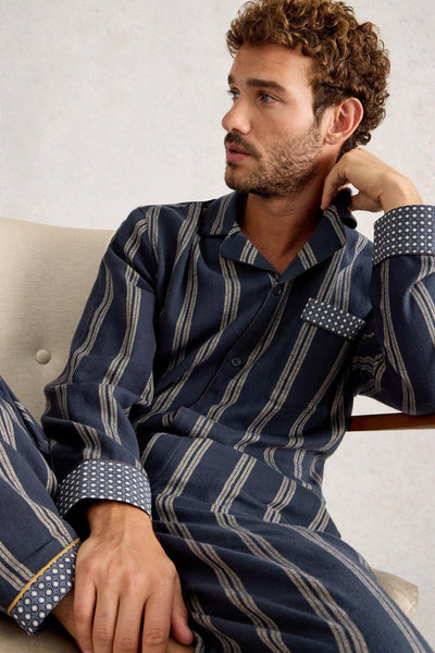 Man wearing a navy and gray striped pajama set sitting on a couch.