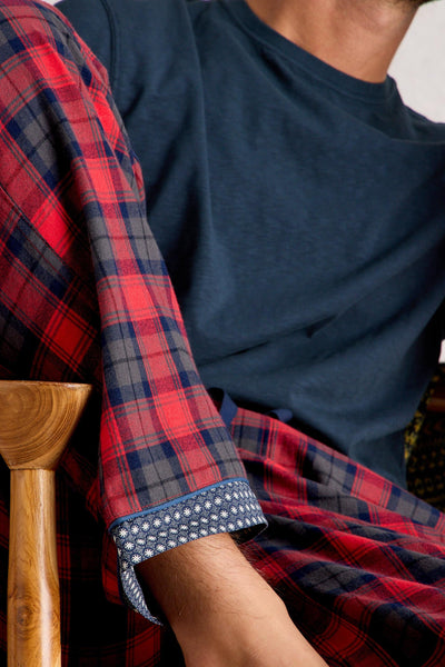 Person wearing a red and blue plaid pyjamas with a navy t-shirt, sitting on a wooden chair.