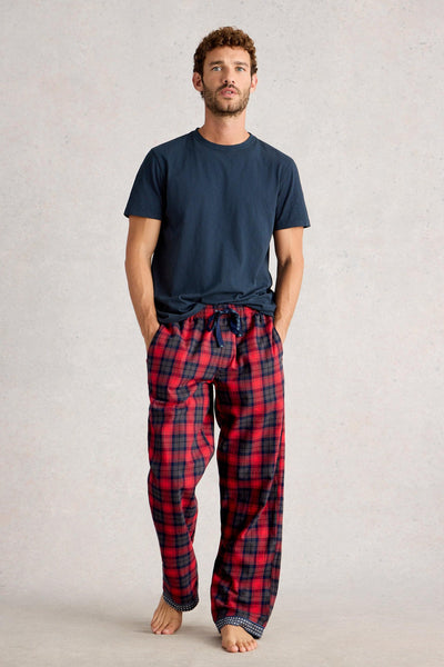 Man wearing a navy t-shirt and red plaid pajama pants on a light gray background
