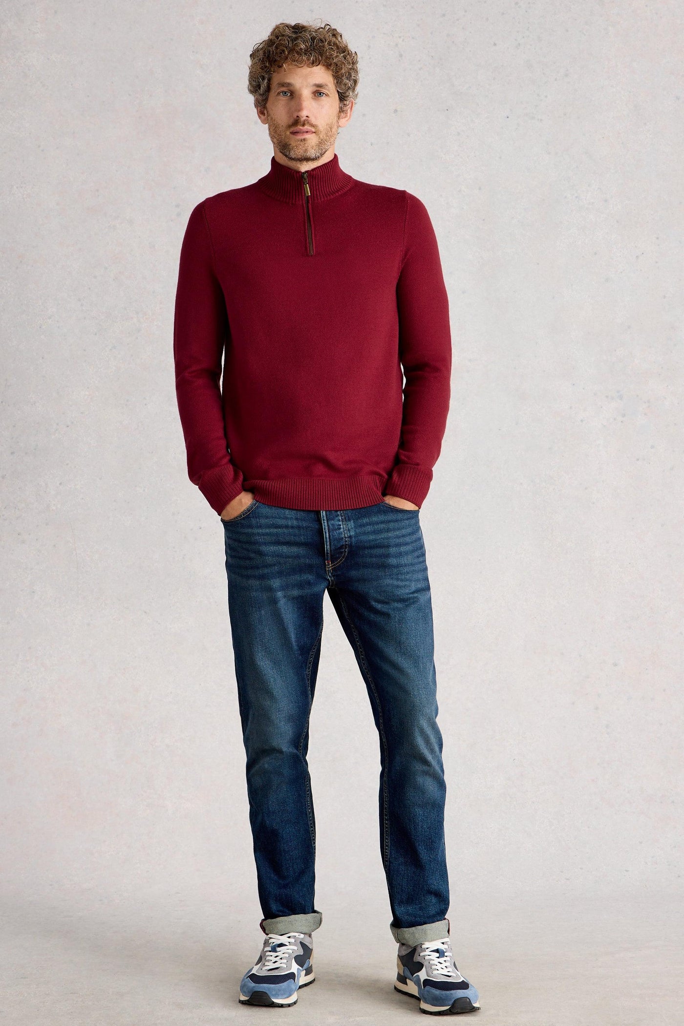 Man wearing red merino long sleeve knit styled with blue denim jeans and blue trainers