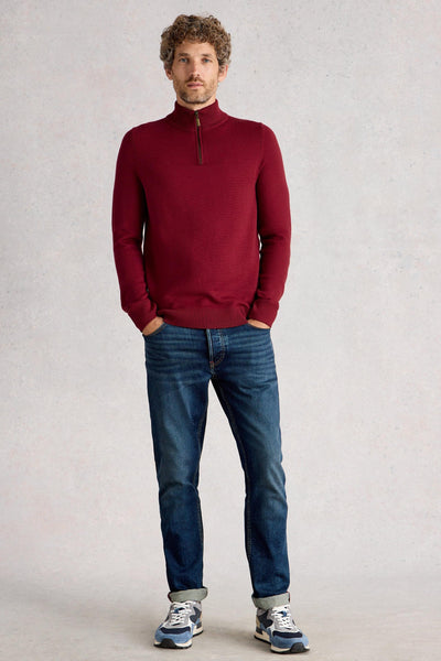 Man wearing red merino long sleeve knit styled with blue denim jeans and blue trainers