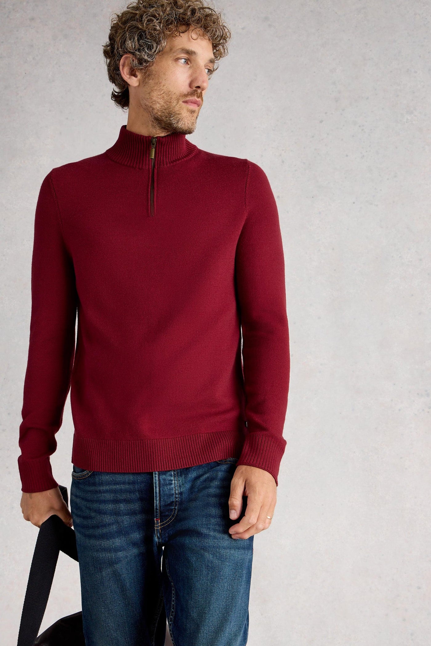 Man wearing a red merino wool long-sleeve knit with a quarter-zip neck, styled with blue denim jeans
