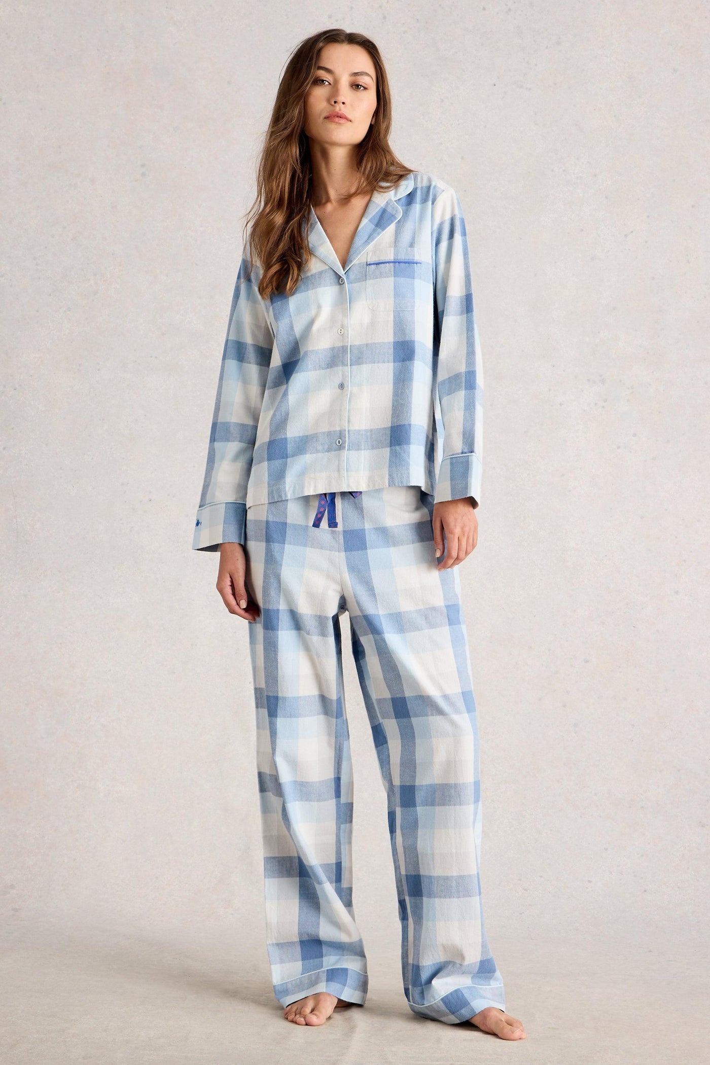 Woman wearing blue and white checkered organic cotton pajamas on a plain background