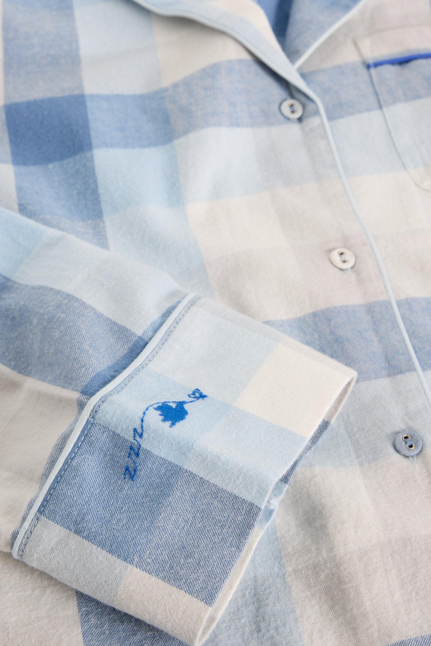 Close-up of a blue and beige checkered shirt with a small logo on a light background